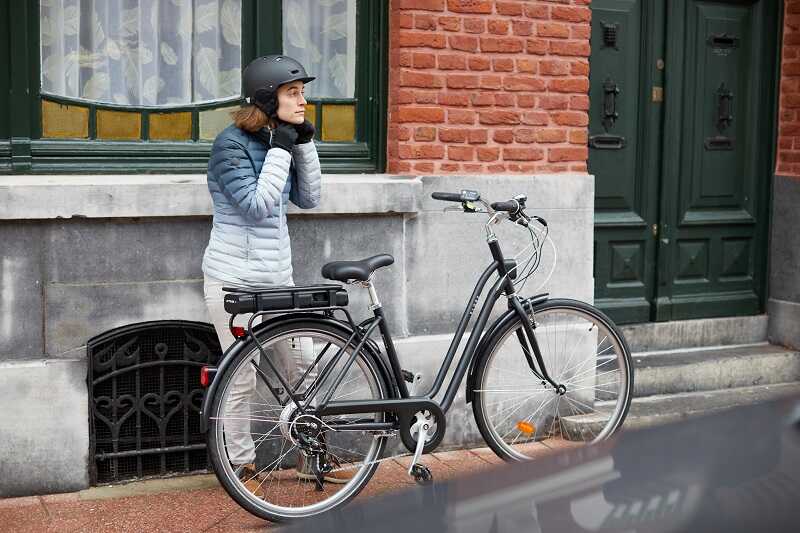 kobieta zapina kask rowerowy i stoi obok czarnego rowera elektrycznego