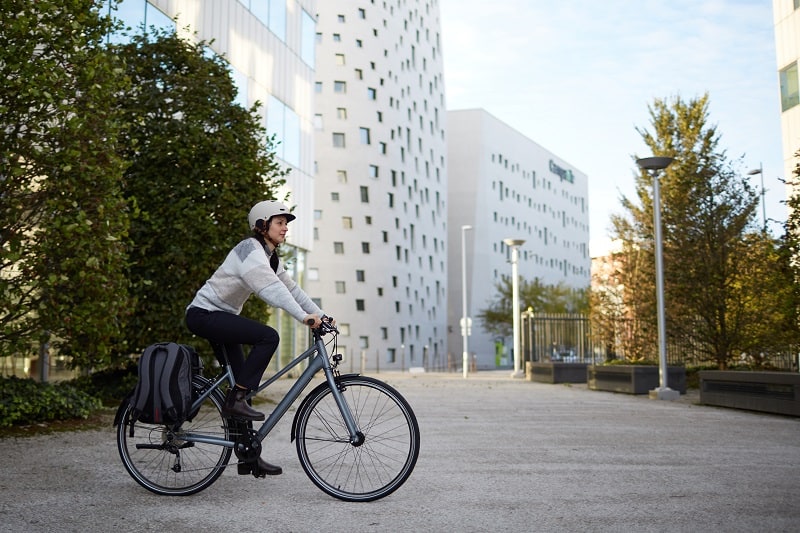 Kobieta w białym kasku siedzi na rowerze miejskim