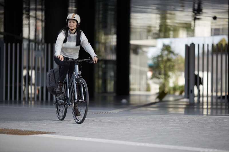 Kobieta w białym swetrze i białym kasku jedzie rowerem miejskim