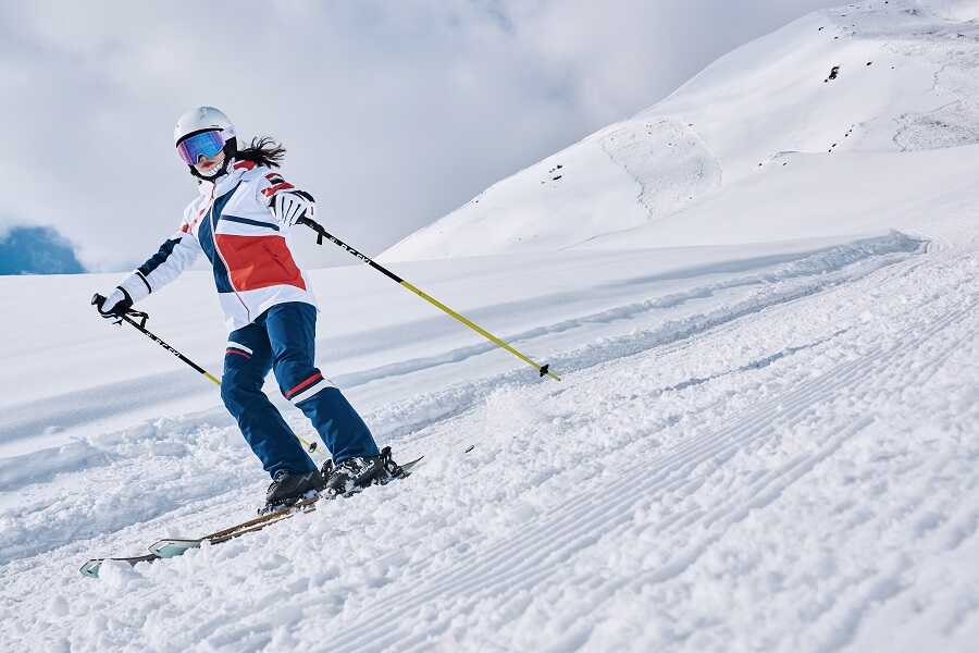 dziewczynka zjeżdża na nartach ubrana w kask narciarski i strój narciarski