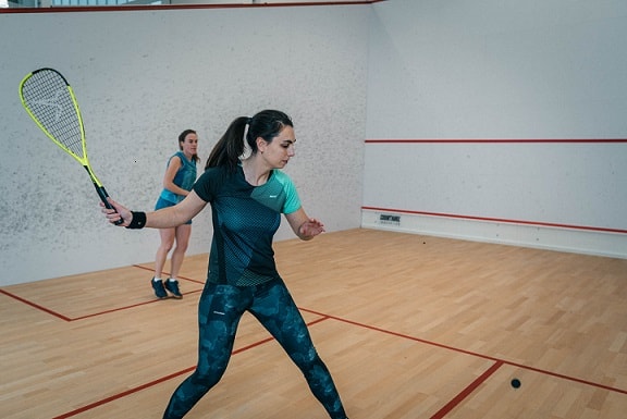kobiety grające sprzętem do squasha na korcie
