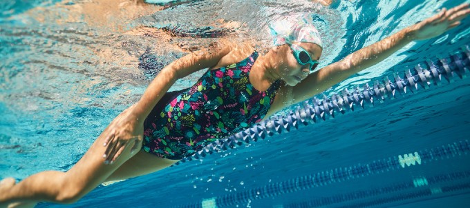 kobieta pływająca na basenie w czepku i goglach pływackich