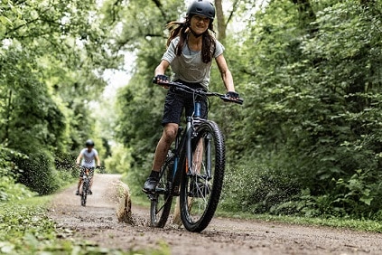 dziewczynka jadąca na rowerze w kasku przez las
