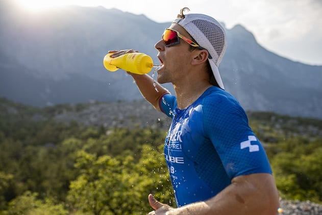 mężczyzna w czapce z daszkiem i okularach przeciwsłonecznych pijący wodę z bidonu