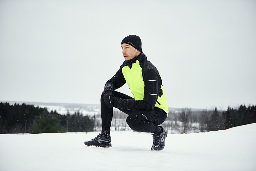 mężczyzna kucający na śniegu w stroju do biegania 