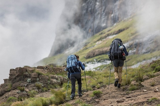 kobieta i mężczyzna idący po górach w butach trekkingowych z kijkami w rękach